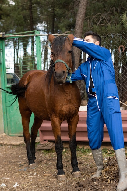 Vertical portrait of young male rancher putting the reins on his mare's or horse's head (Equus ferus caballus)