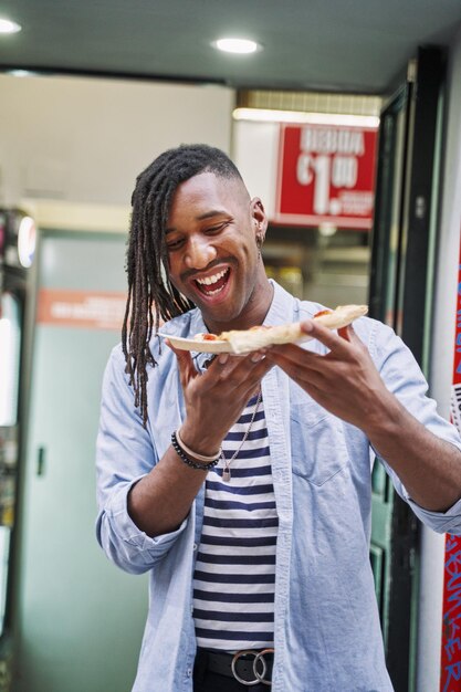 vertical portrait of a young man eating a slice of takeaway pizza