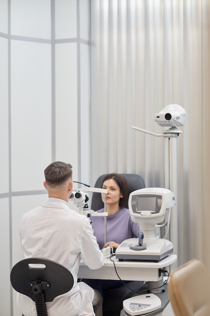 現代の眼科クリニックでの視力検査中に機械を使用している若い女性の縦の肖像画