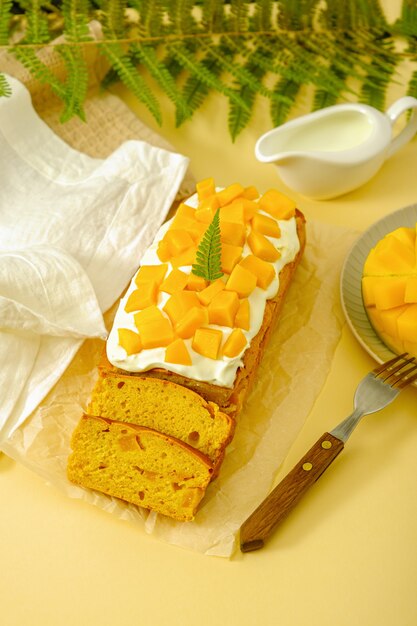 Vertical pound cake with mango and whipped cream on yellow background, home cooking, mango desserts