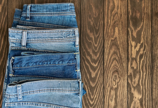 Vertical row of fashionable different jeans on a wooden background with copy space