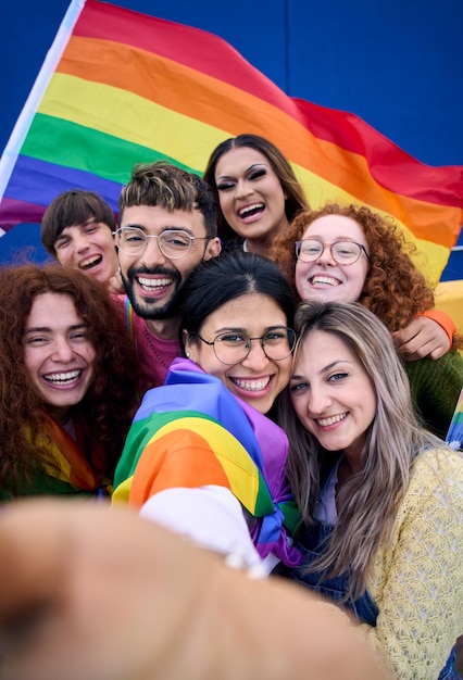 Foto selfie verticale di giovani lgbt che festeggiano la giornata dell'orgoglio gay tenendo insieme la bandiera dell'arcobaleno