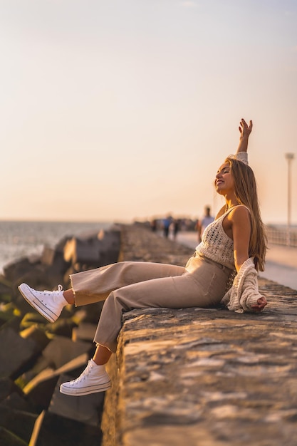 Vertical shallow focus shot of a young blonde Caucasian female during sunset by the beach near sea