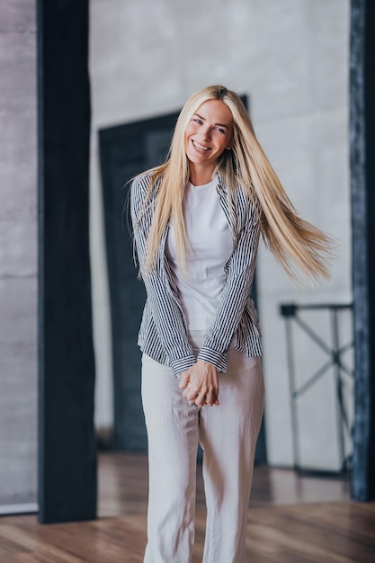 Vertical shoot of blonde Swedish girl in casual laughing comes in new apartment with fluttering hair