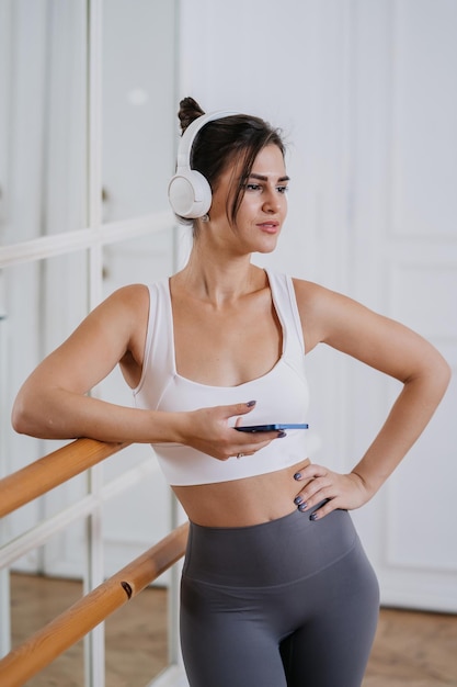 Foto tiro verticale di ragazza ispanica castana in abbigliamento sportivo alla pausa dell'allenamento in palestra utilizzando le cuffie