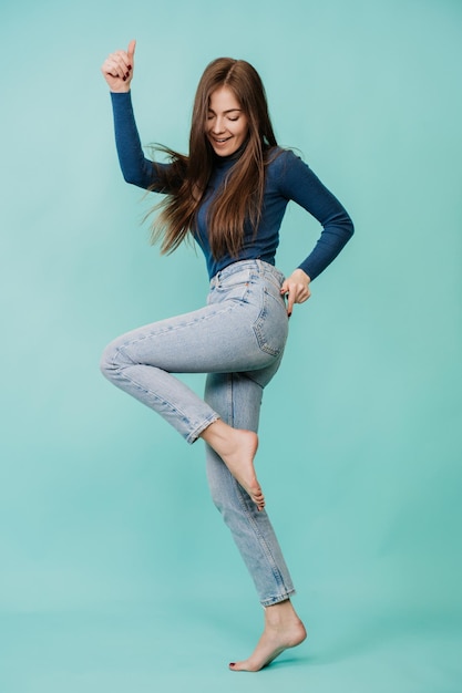 Vertical shoot of dancing beautiful Italian young woman in blue sweater blue jeans over turquoise