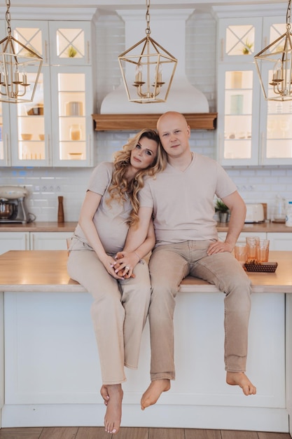 Vertical shoot of Swedish bald man in casual sitting with pregnant attractive wife on kitchen table