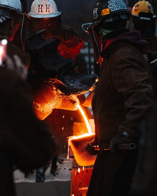 Vertical shot of adult industrial workers in uniforms melting metal in a factory