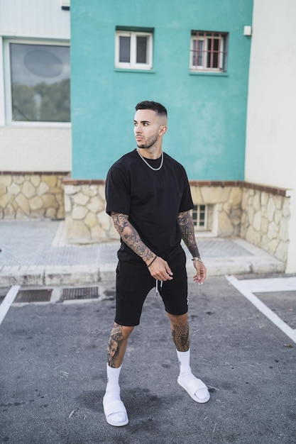 Vertical shot of an athletic young man with tattoos posing standing on the street