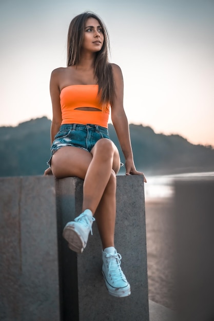 Vertical shot of an attractive brunette sitting on a concrete surface