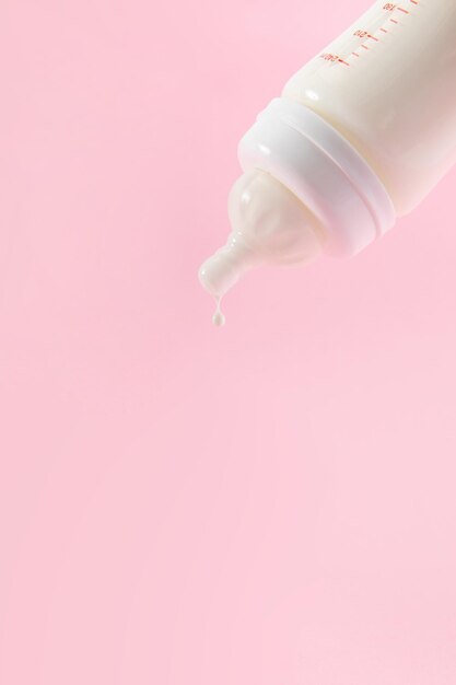 Vertical shot of a baby bottle full of milk on pastel pink background for a copy space