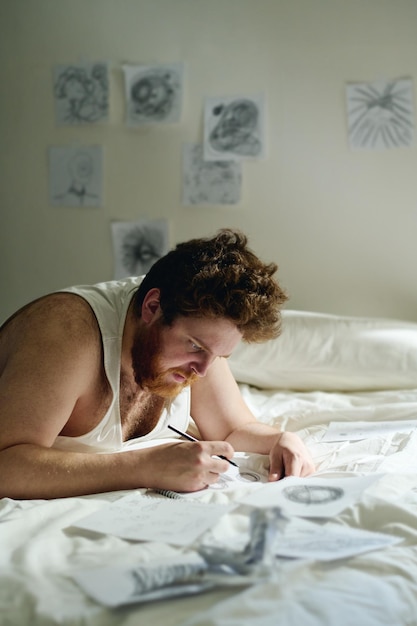 Vertical shot of bearded male patient of mental hospital drawing with pencil