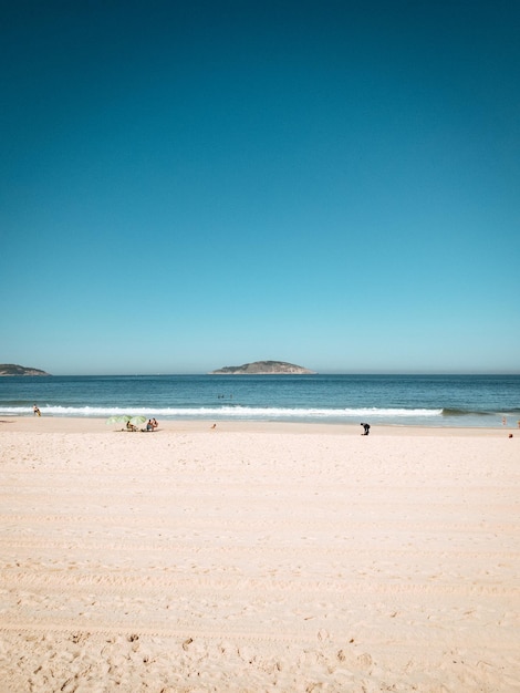 Вертикальный снимок красивого песчаного пляжа под голубым ясным небом