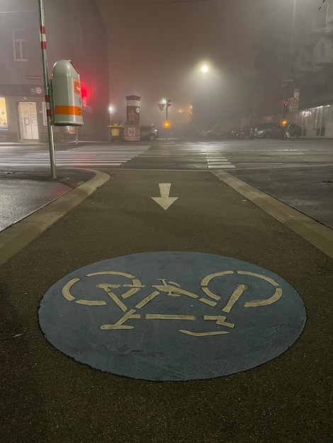 Vertical shot of a bicycle lane sign painted on concrete empty\
city streets in fog on background