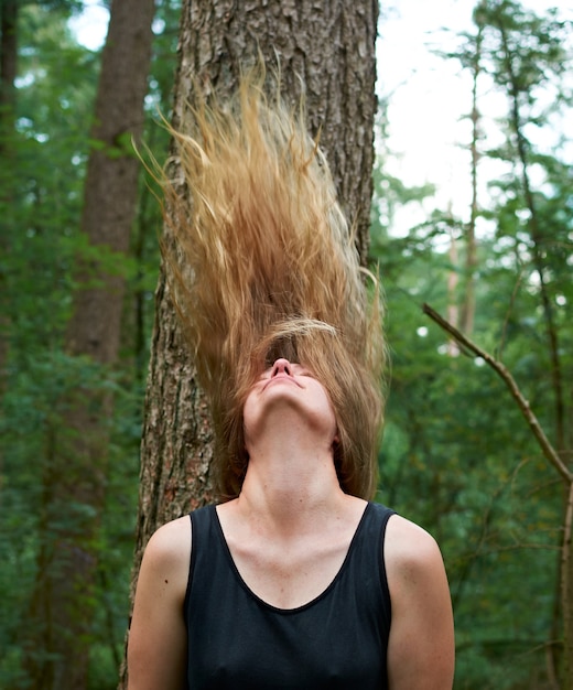 Foto un colpo verticale di una bionda caucasica con i suoi lunghi capelli in aria nella foresta