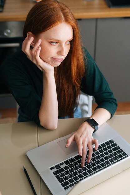 Inquadratura verticale di una giovane donna annoiata che digita sulla tastiera del laptop tenendo la mano sul mento seduta distogliendo lo sguardo frustrata freelance che sente mancanza di motivazione infastidita dalla noia e dal lavoro noioso