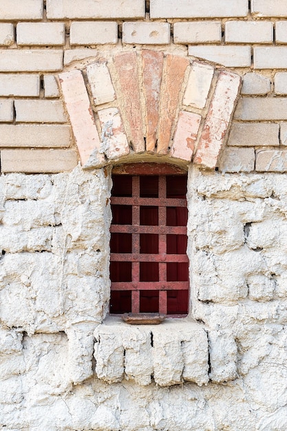 Vertical shot of a brick wall with a small old barred window