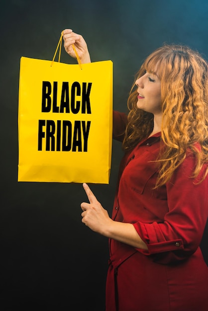 Foto ripresa verticale di una donna caucasica che mostra una borsa della spesa su sfondo nero venerdì nero