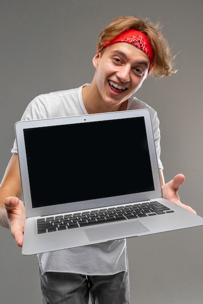 회색 격리 된 배경에 치아와 넓은 미소로 앞으로 빈 화면이 노트북과 두건에 쾌활한 남자의 세로 샷