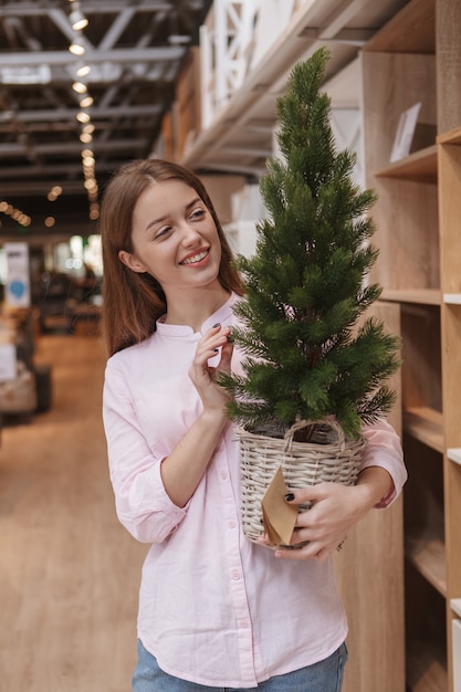 Vertical shot of a cheerful woman buying x-mas tree at home goods supermarket