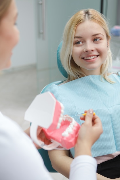 Colpo verticale di una giovane donna allegra sorridente al suo dentista seduto in poltrona odontoiatrica