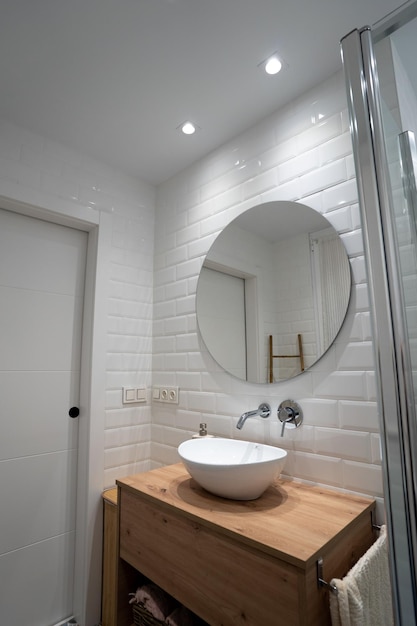 Вертикальный снимок кругового зеркала на белой стене с раковиной и водяным краном внизу в ванной