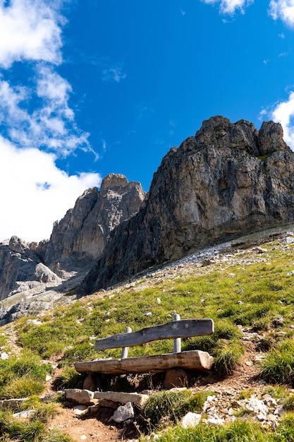 Vertical shot of cliffs with a wooden bench at the bottom under the blue sky in the Dolomites Italy