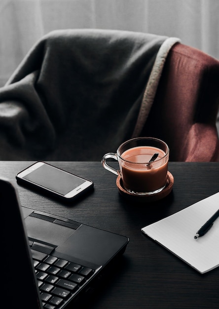 Vertical shot of a cup of coffee on work desk with laptop and smartphone