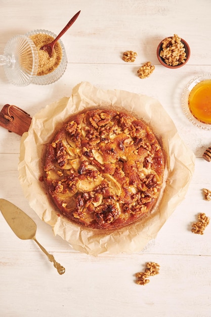 Vertical shot of a delicious apple walnut cake with honey surrounded by ingredients on a white table