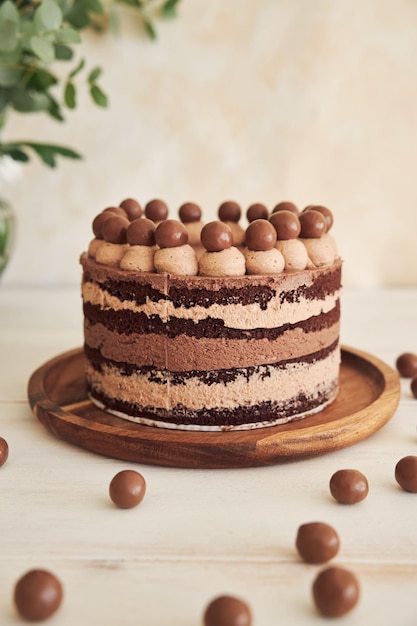 Vertical shot of a delicious chocolate naked cake with choco balls and cream on a white table