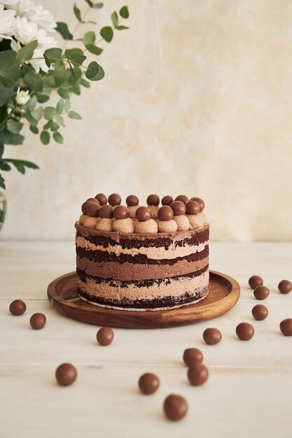 A vertical shot of a delicious chocolate naked cake with choco balls and cream on a white table