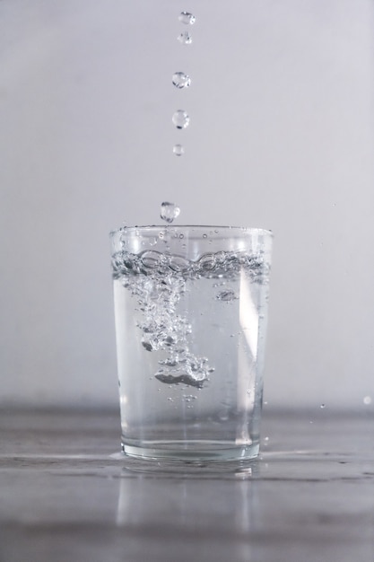 Вертикальный снимок капли воды в стеклянную чашку