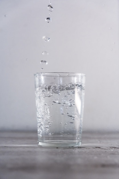 Vertical shot of dropping water into a glass cup