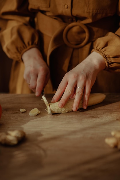 Vertical shot of female hands cutting banana on a wooden surface