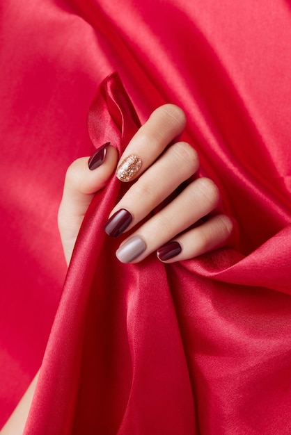 Vertical shot of a females hand with beautiful nail polish caressing a red silk fabric