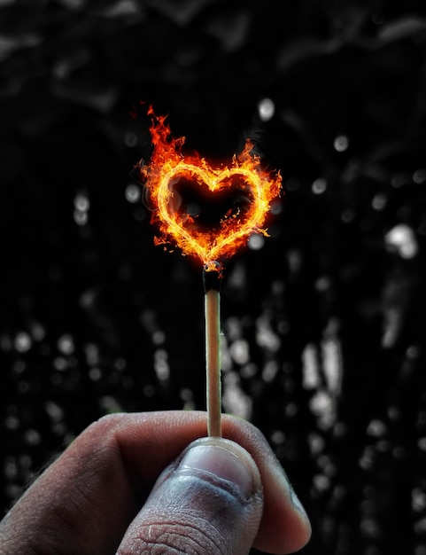 Вертикальный снимок руки, держащей спичку с горящим огнем в форме сердца