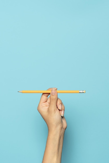 Foto colpo verticale di una mano che tiene una matita isolata su sfondo blu