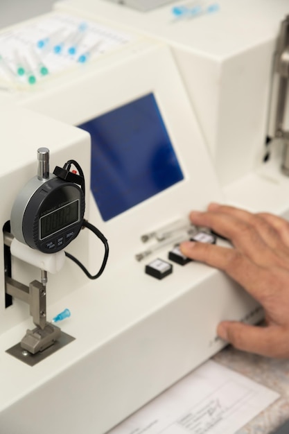 A vertical shot of a hand using a medical machine to test and manufacture pharmaceutical syringes