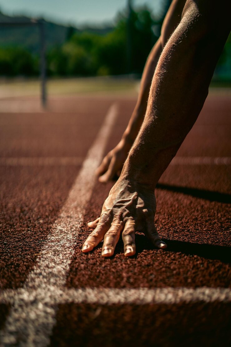 Photo vertical shot of the hands in a starting position on an athletics track