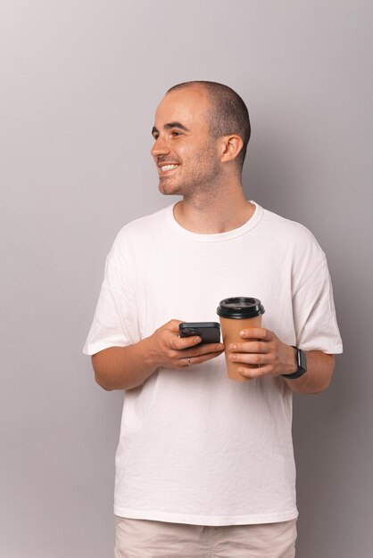 Vertical shot of a handsome young bald man holding phone and to go coffee cup