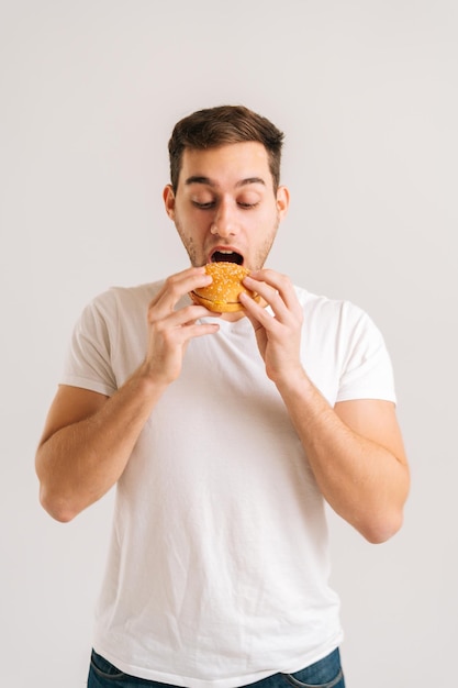 白い孤立した背景でおいしいハンバーガーを食べることを楽しんでハンサムな若い男の垂直ショット