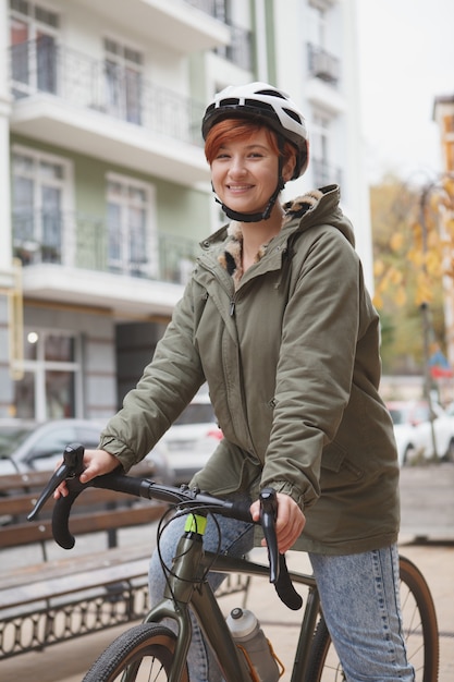 Colpo verticale di una giovane donna felice che indossa il casco da bici in bicicletta in città