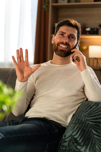 Photo vertical shot of the happy youthful businessman making freelance work at his room and having call via smartphone