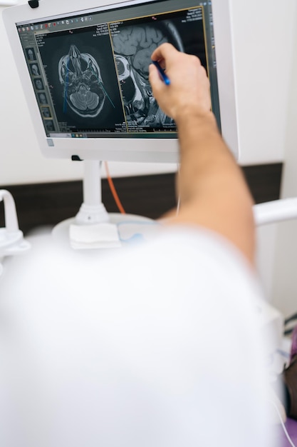 Photo vertical shot of male dentist pointing at teeth radiography on monitor to explain dentition