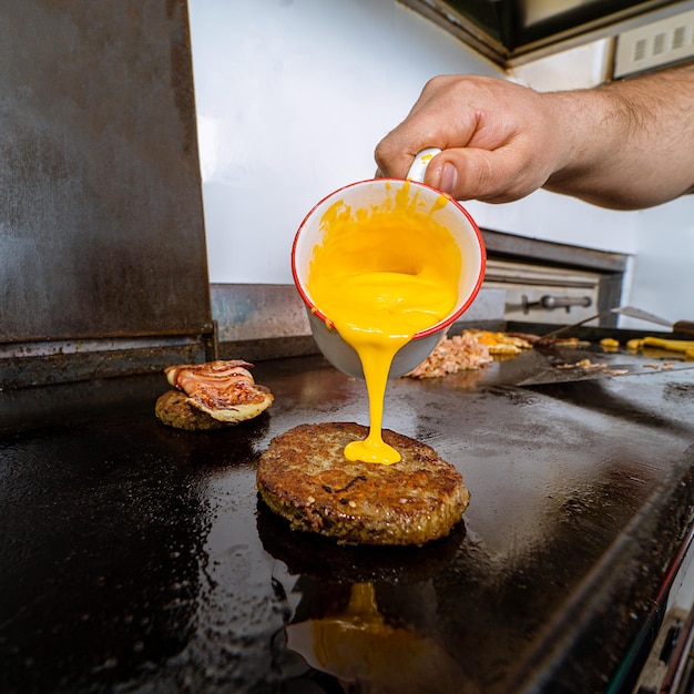 Vertical shot of a male\'s hand pouring cheese on a cutlet on\
the grill