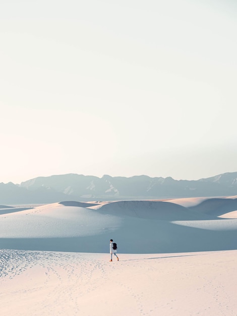 Vertical shot of a man and the picturesque landscape of dim white dunes sands during sunset