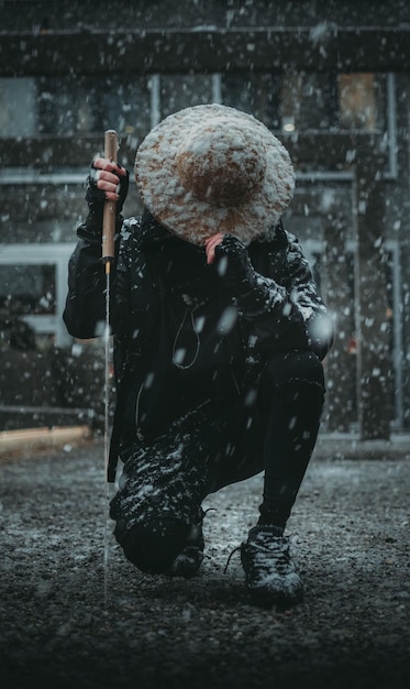 Vertical shot of a man with a Sword and Asian hat on his nee under the snow