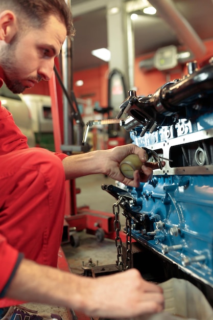 Foto foto verticale di un meccanico in uniforme rosso che monta il motore c e lubrifica