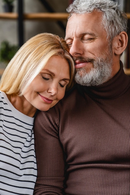 Vertical shot of middle aged couple in love hugging on sofa at home