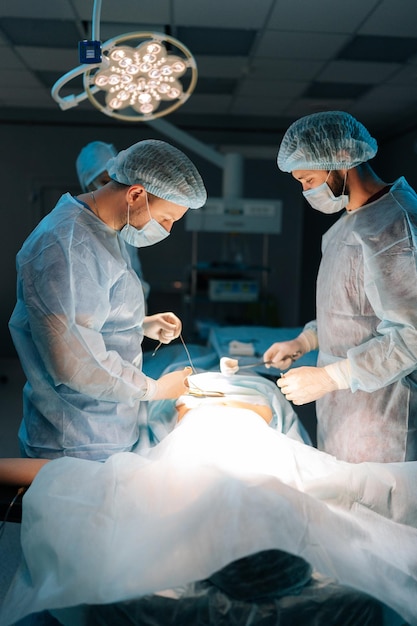 전문적인 남성 외과 의사와 여성 간호사의 다민족 팀이 침습적인 수술을 수행하는 수직 